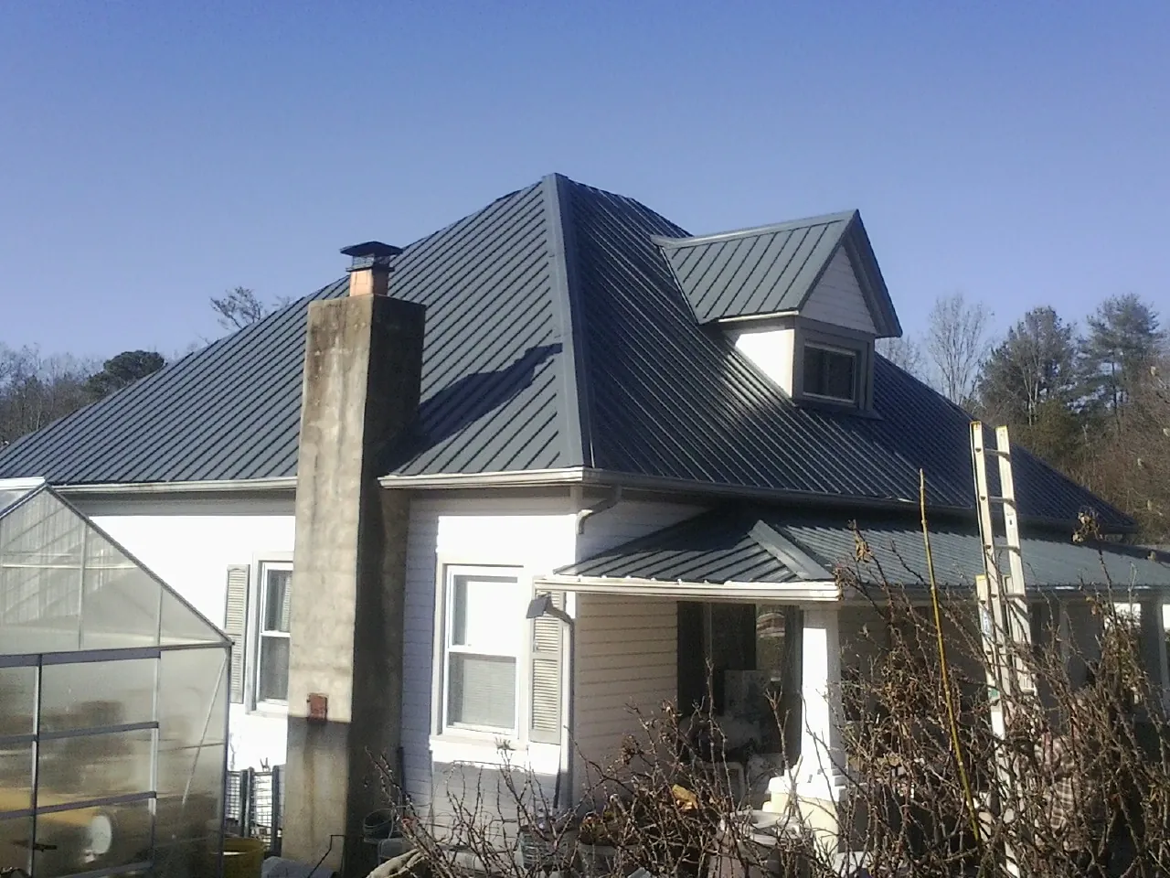 Dark blue standing seam metal roof on a white farmhouse with dormer — Slate & Tile Roof Repair by Roofing Brothers in Coleman