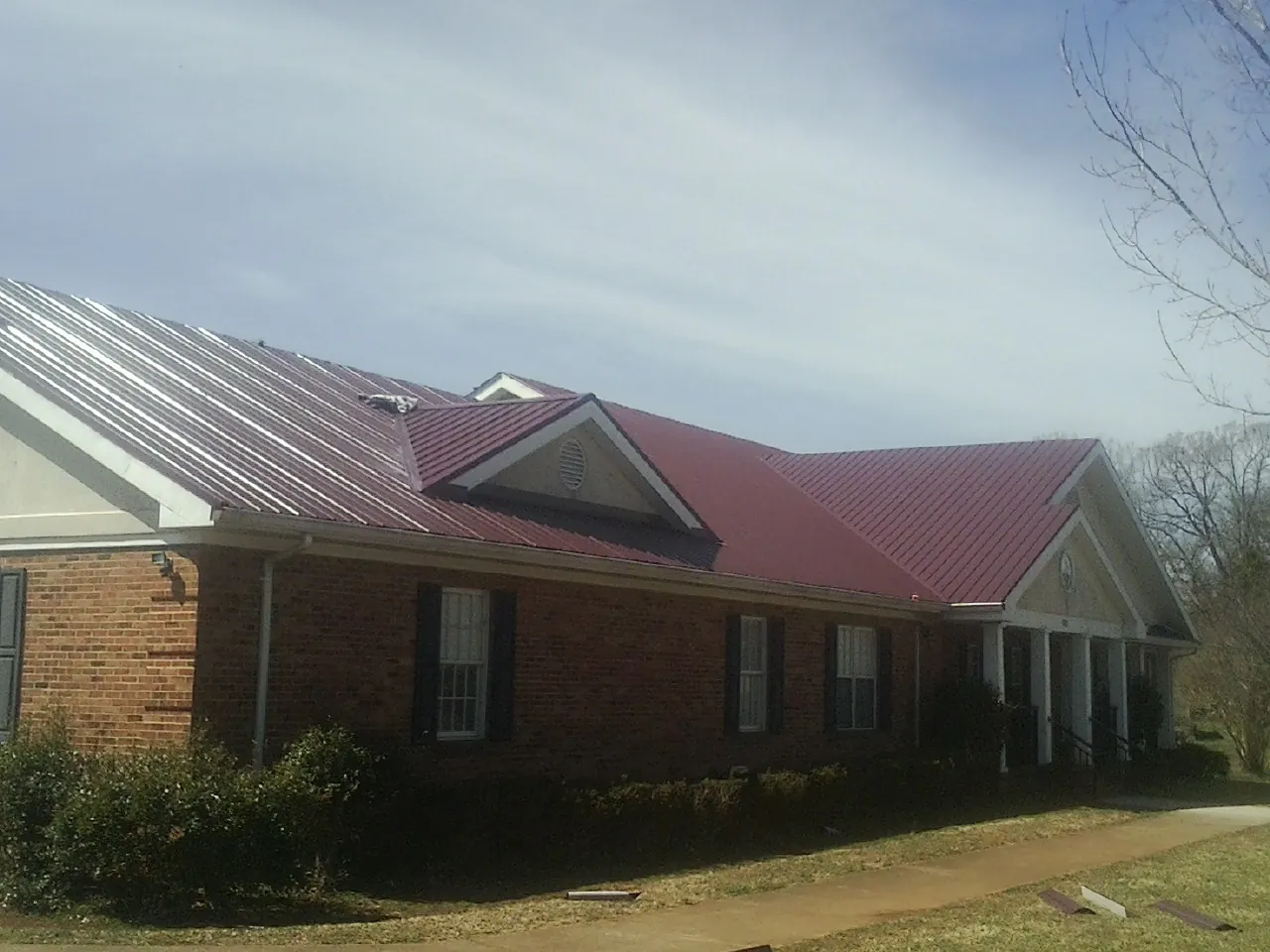 Red metal roof with gabled entries on a long brick building, from a Hail Damage Roof Repair job in Coleman