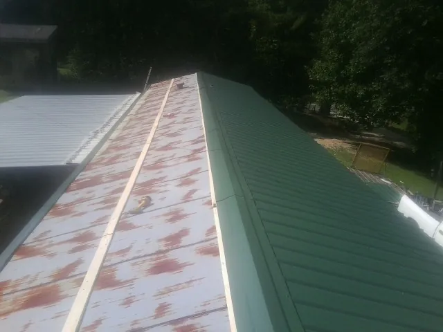 Old rusted panels beside newly installed green metal roofing — Wind Damage Roof Repair by Roofing Brothers in Coleman