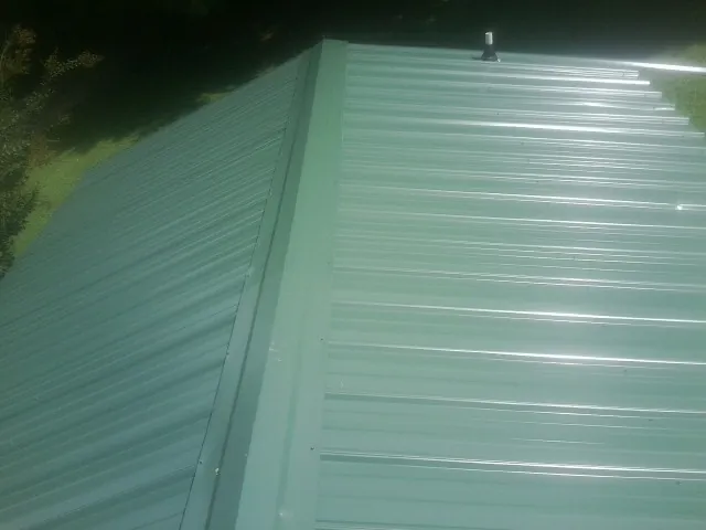 New green metal panels meeting at the ridge of a roof — Flat Roof Repair work by our crew in Coleman