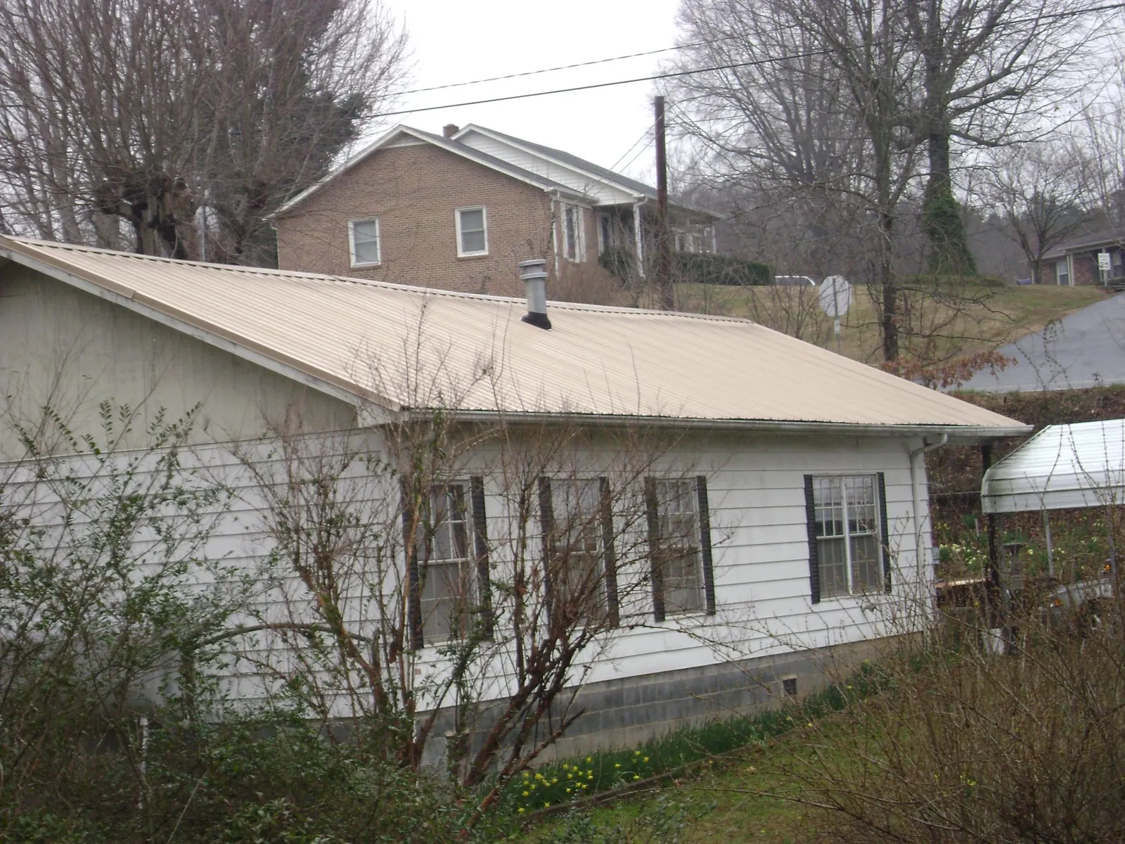 Tan metal roof on a white sided house set into a hillside — Commercial Roofing by Roofing Brothers in Coleman